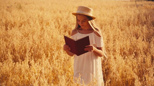 girl in white dress and straw hat reading book in wheat field