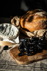 Still life with Camembert, blue grapes and whole round bread loaf on linen tablecloth 