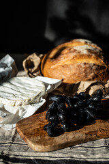 Still life with Camembert, blue grapes and whole round bread loaf on linen tablecloth 