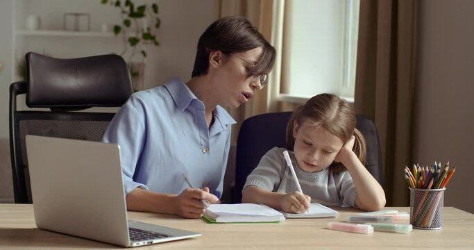 Cute small preschool girl kid daughter learning writing with young mom tutor. Adult parent mother teaching school child helps with homework studying sitting at home table. Children education concept