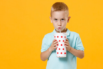 Smiling little fun male fair-haired brown-eyed kid boy 5-6 years old wearing stylish blue t-shirt polo hold paper cup of drink cola soda isolated on yellow color wall background child studio portrait.