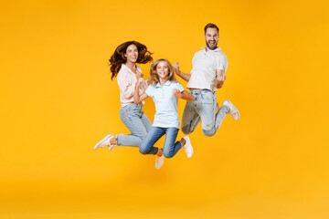 Fototapeta na wymiar Full length portrait of happy young parents mom dad with child kid daughter teen girl in basic t-shirts jumping doing winner gesture isolated on yellow background studio portrait. Family day concept.
