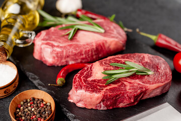 Fototapeta na wymiar Two raw marbled beef ribeye steaks with spices on a stone background