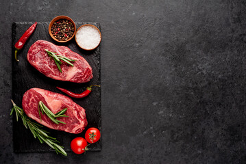 Two raw beef ribeye steaks with spices on stone background with copy space for your text