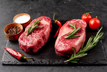 Two raw beef ribeye steaks with spices on stone background with copy space for your text
