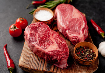 Two raw beef ribeye steaks with spices on a stone background