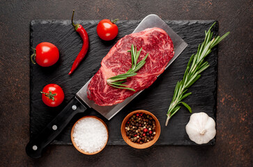 Raw beef rib eye steak on a meat knife on stone background with copy space