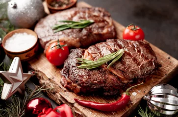 Fotobehang Christmas dinner for two, grilled beef steak ribeye, herbs and spices on a stone table with a Christmas tree and New Year's toys  © александр таланцев