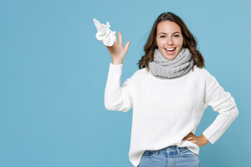 Cheerful funny young woman wearing white sweater gray scarf throwing out paper napkin isolated on blue background studio portrait. Healthy lifestyle ill sick disease treatment cold season concept. - obrazy, fototapety, plakaty