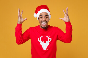 Fototapeta na wymiar Angry young Santa african american man in red sweater Christmas hat spreading hands screaming swearing isolated on yellow background studio portrait. Happy New Year celebration merry holiday concept.