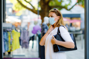 Portrait of young beautiful woman wearing medical mask as protection against corona virus. Woman shopping in the city. Covid pandemic time in Europe and in the world. Safety for people.