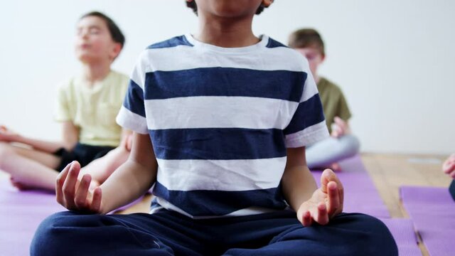 Close up on hands as group of boys sit on exercise mats and meditate in yoga studio - shot in slow motion 