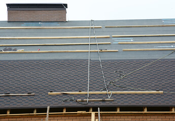 A close-up on a roof under construction with asphalt shingles installation on felt paper or underlayment with safety roof harness and ropes that were left by roofing contractors.