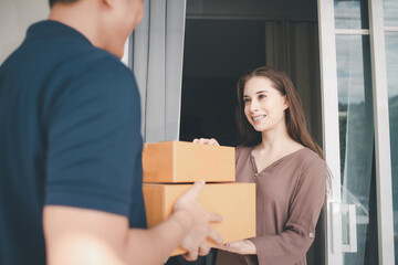 Asian deliver man in blue uniform handling package box to Caucasian female costumer in front of the house