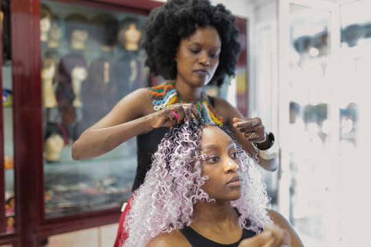 A black hairdresser making the crochet style with a crochet hook to a young black client.