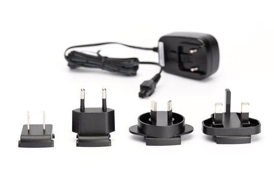Four black interchangeable plugs for Europe, Australia and Great Britain with a black plug-in power supply in the background