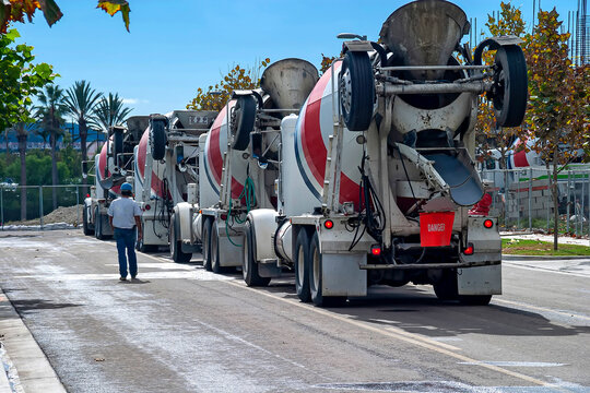 Row of cement trucks at a job sirte with a worker in hardhat standing near the trucks