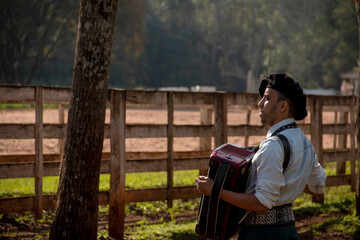Young man playing the accordion in profile on a horse ranch.