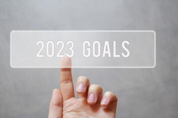 2023 goals - finger pressing grey transparent button on gray virtual touchscreen interface. New year resolutions planning concept.
