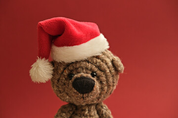 Funny handmade bear toy in small Santa`s hat on red christmas background