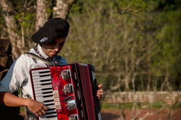 Gaucho boy with typical costumes playing the harmonica outdoors.