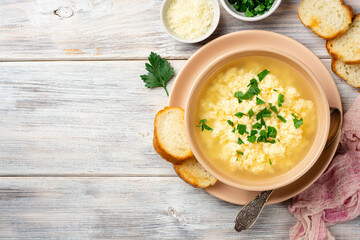 Italian stracciatella egg drop soup with parmesan cheese and parsley in bowl on rustic wooden background
