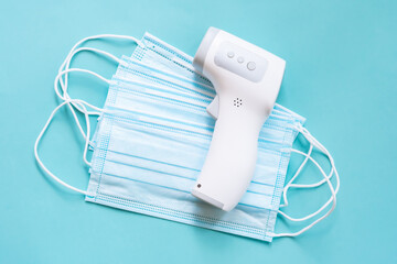 Digital infrared thermometer is lyiing on stack of medical masks on blue background. Health...