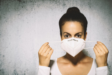 Close-up photo of young brunette woman putting on protective mask.