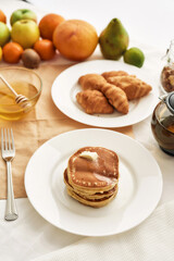 Close up of sweet tasty pancakes, croissants, honey in a bowl and various fruits, Breakfast served on the table