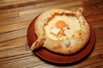 Top view on traditional Adjarian Khachapuri - open baked pie with melted salt cheese suluguni and egg yolk on wooden tray. Traditional georgian food