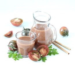 Black tomato juice in a jug and glass with bamboo straws on a light background