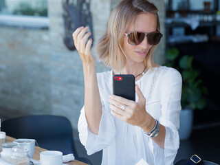 Woman is sitting in a cafe straightening her hair and looking at camera smartphone.