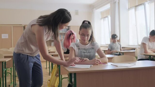 Lesson in class, young female teacher teaches teenage girl, group of schoolchildren background