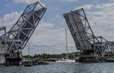 Fototapeta na wymiar Drawbridge Up: A bridge designed to separate at the middle raises its two sides to allow passage of a sailboat through the harbor at Sturgeon Bay, Wisconsin. 