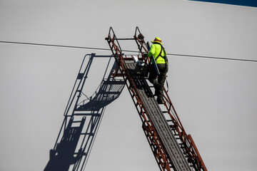 Painter wearing a hat on a ladder casting a shasow on a white commercial building