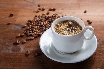 White cup of coffee on a wooden table next to a scattering of coffee beans.