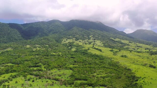 Exotic tropical landscape of the island of Saint Kitts, West Indies, in the Caribbean sea, with green plains and forests, tall mountains covered with trees, large clouds above. Scenic aerial shot 4K.