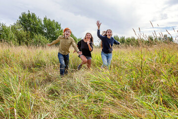 Summer holidays vacation happy people concept. Group of three friends boy and two girls running and having fun together outdoors. Picnic with friends on road trip in nature.