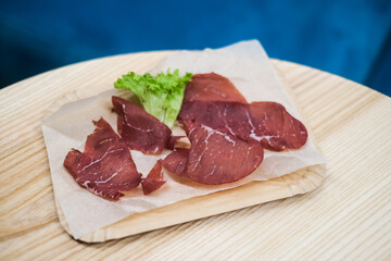 Meat smoked jerky - raw meat sausage meat. Close up view on tasty sliced Chicken basturma on paper plate on a wooden background . Beer snack. Pastirma