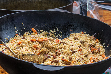 Healthy street food to go - in a large cauldron hot pilaf with pieces of meat and whole hot red pepper. Delicious food cooked over an open fire, which is offered at a street food fair, event, festival
