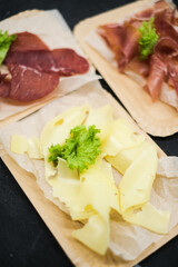 Cheese slices. Meat smoked jerky - raw meat sausage meat. Close up view on tasty sliced Chicken basturma on paper plate on a wooden background . Beer snack. Pastirma