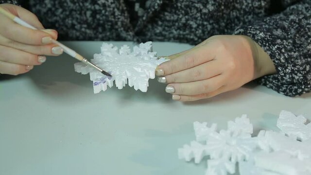 Woman's hands on a winter evening makes home decorations for Christmas by painting figures with watercolors