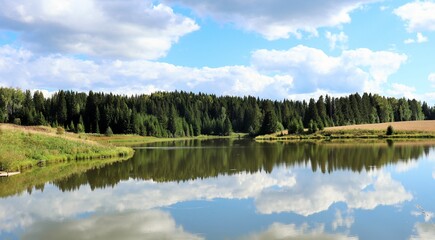 Fototapeta na wymiar Forest lake on a sunny day with reflective clouds