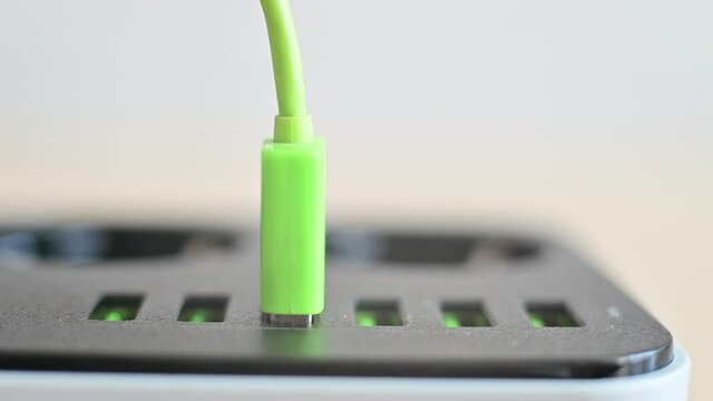 Modern convenient multi-port usb charger for devices. Close-up of a female hand plugging multi-colored cables into a power outlet. Macro.