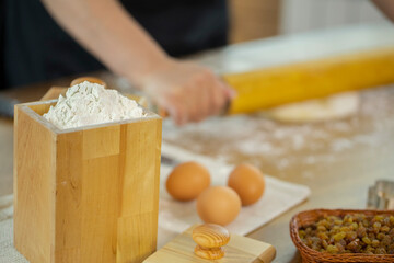 Wheat flour in wooden jar and eggs on oak kitchen table. Caucasian housewife rolls out the pizza dough with a rolling pin. Concept of home baking. Quarantine time.