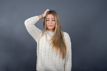 Beautiful young blonde woman wearing white sweater standing against gray background, 