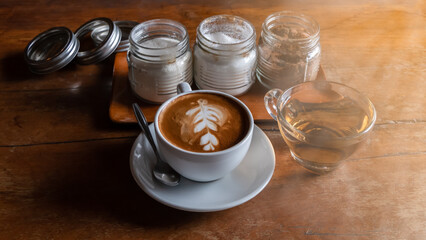Black coffee in a white cup is placed on the table with a glass of tea, sugar and creamer.