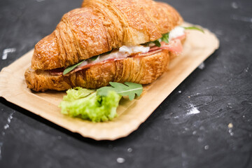 Croissant with ham and cheese arugula and lettuceon, in a paper plate top view