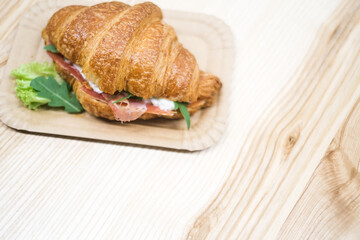Croissant with ham and cheese arugula and lettuceon, in a paper plate top view