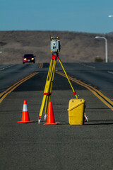 Land survey equipment set up on road with road becoming a hill in the background with traffic